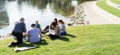 Students and Professor talking with notebooks and books near a pond.